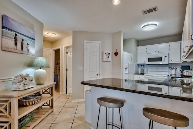 kitchen featuring dark stone countertops, white cabinets, white appliances, and kitchen peninsula