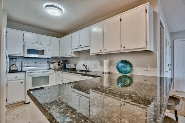 kitchen with sink, white appliances, dark stone countertops, white cabinetry, and a textured ceiling