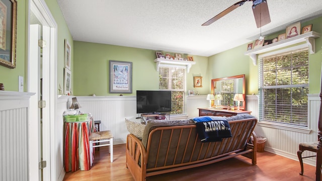 living room with ceiling fan, a textured ceiling, and light wood-type flooring