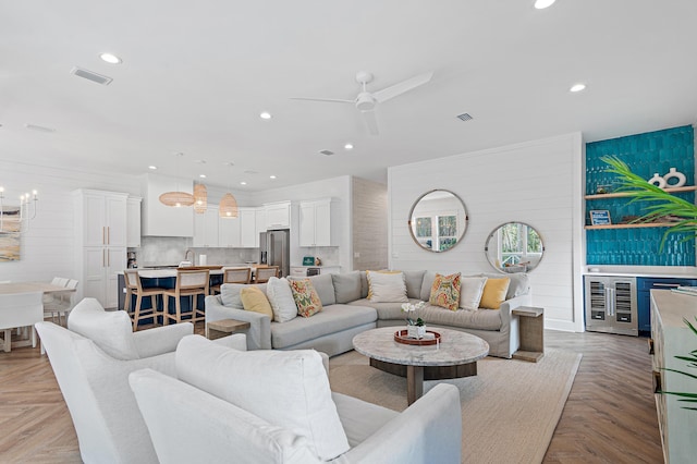 living room featuring light parquet flooring, ceiling fan with notable chandelier, and beverage cooler