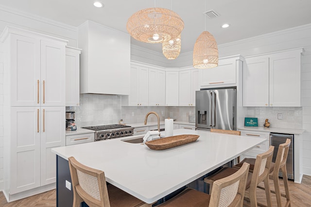 kitchen featuring pendant lighting, appliances with stainless steel finishes, white cabinets, a center island with sink, and beverage cooler