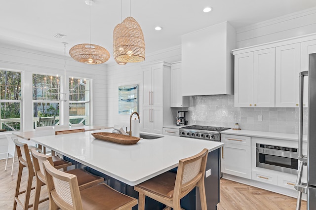 kitchen with hanging light fixtures, an island with sink, sink, and white cabinets