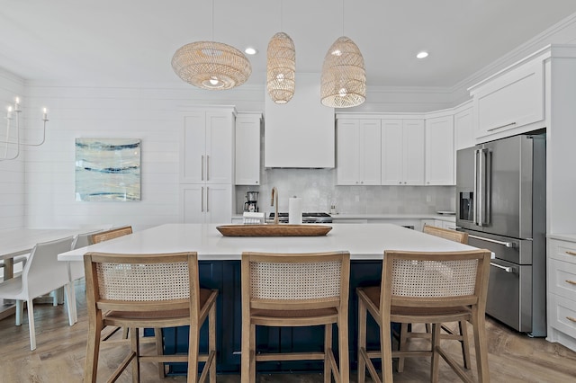 kitchen with sink, high quality fridge, pendant lighting, a kitchen island with sink, and white cabinets