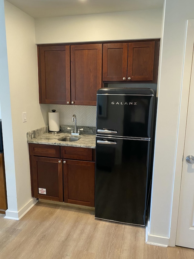 kitchen featuring light stone countertops, black refrigerator, sink, and light wood-type flooring