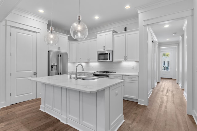 kitchen featuring appliances with stainless steel finishes, sink, white cabinets, light stone counters, and a center island with sink