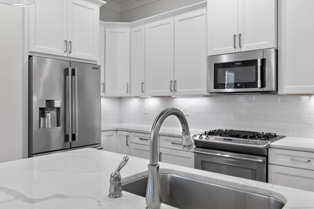 kitchen with stainless steel appliances, tasteful backsplash, light stone countertops, and white cabinets