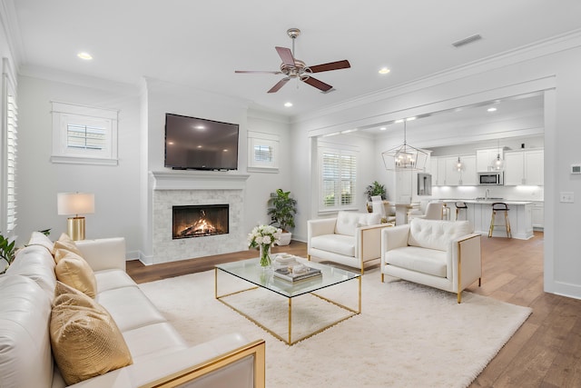 living room featuring crown molding, ceiling fan with notable chandelier, and light hardwood / wood-style flooring