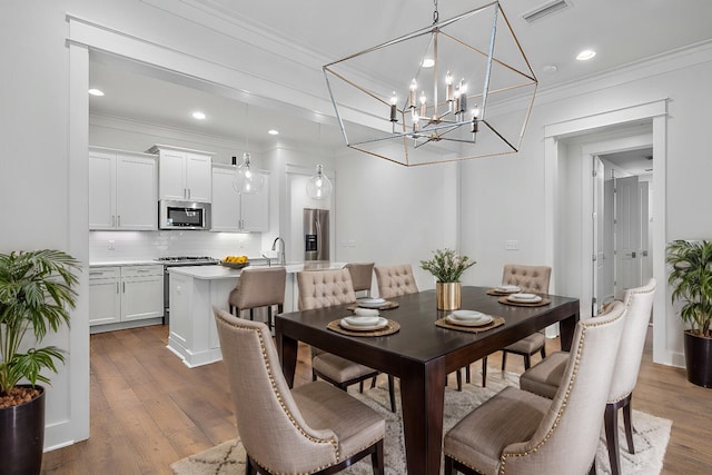 dining area featuring an inviting chandelier, hardwood / wood-style floors, ornamental molding, and sink