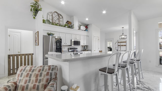 kitchen featuring appliances with stainless steel finishes, a breakfast bar, pendant lighting, white cabinets, and a high ceiling