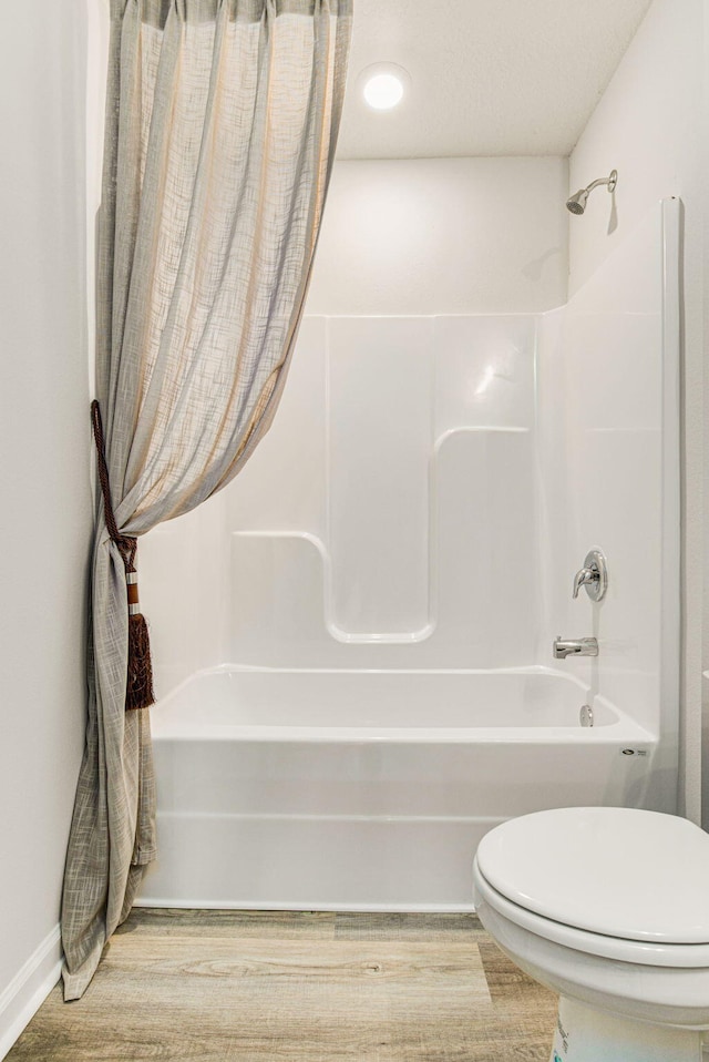 bathroom featuring wood-type flooring, washtub / shower combination, and toilet