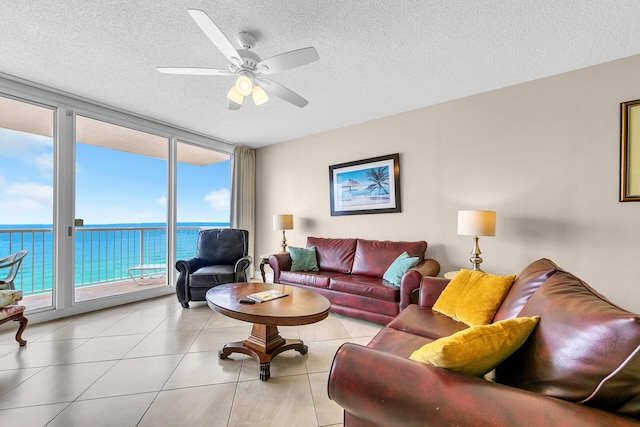 tiled living room with ceiling fan, a water view, a textured ceiling, and a wall of windows