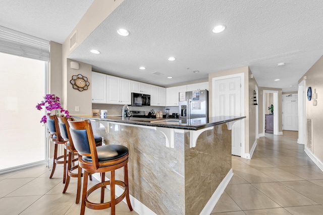 kitchen with white cabinetry, appliances with stainless steel finishes, a kitchen breakfast bar, and light tile patterned floors