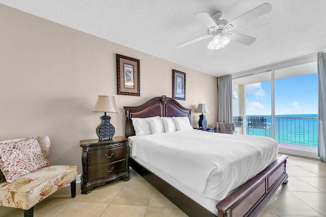 tiled bedroom featuring ceiling fan, a water view, expansive windows, a textured ceiling, and access to outside