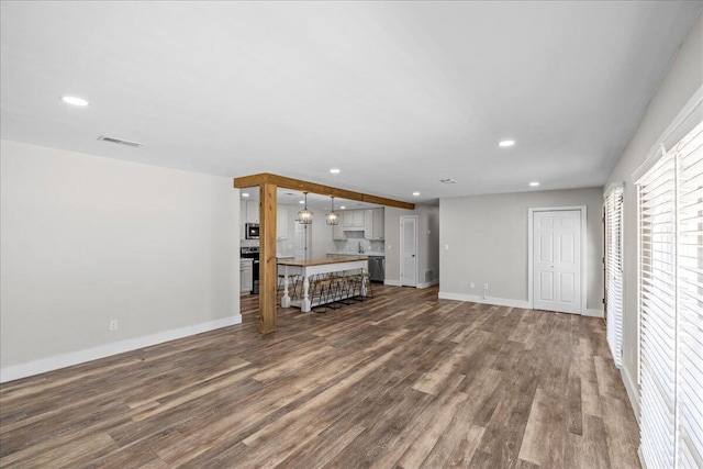 unfurnished living room featuring baseboards, dark wood-style flooring, visible vents, and recessed lighting