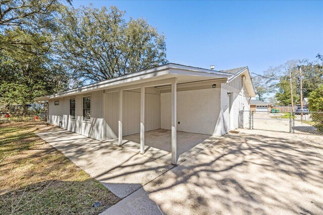 view of home's exterior featuring brick siding, a gate, fence, an attached carport, and driveway