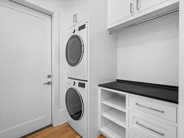 clothes washing area featuring stacked washer and dryer, cabinets, and light wood-type flooring