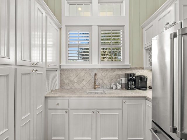 kitchen featuring sink, light stone counters, high end refrigerator, white cabinets, and backsplash