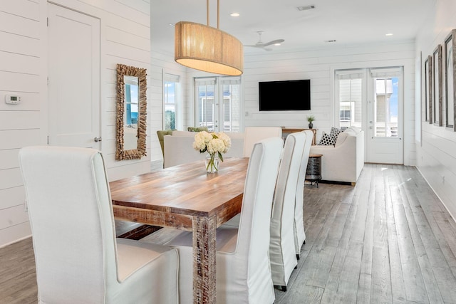 dining space with french doors, wood-type flooring, and wood walls