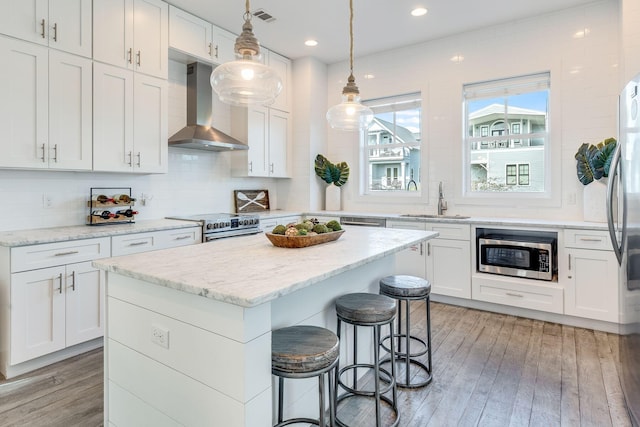 kitchen with white cabinetry, wall chimney range hood, sink, and appliances with stainless steel finishes