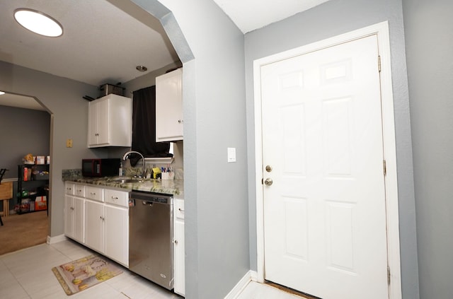 kitchen featuring light tile patterned flooring, sink, dark stone countertops, dishwasher, and white cabinets