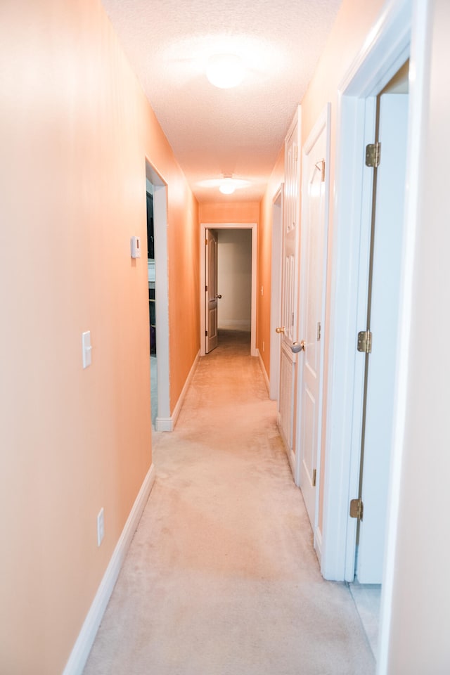 hallway with light carpet and a textured ceiling