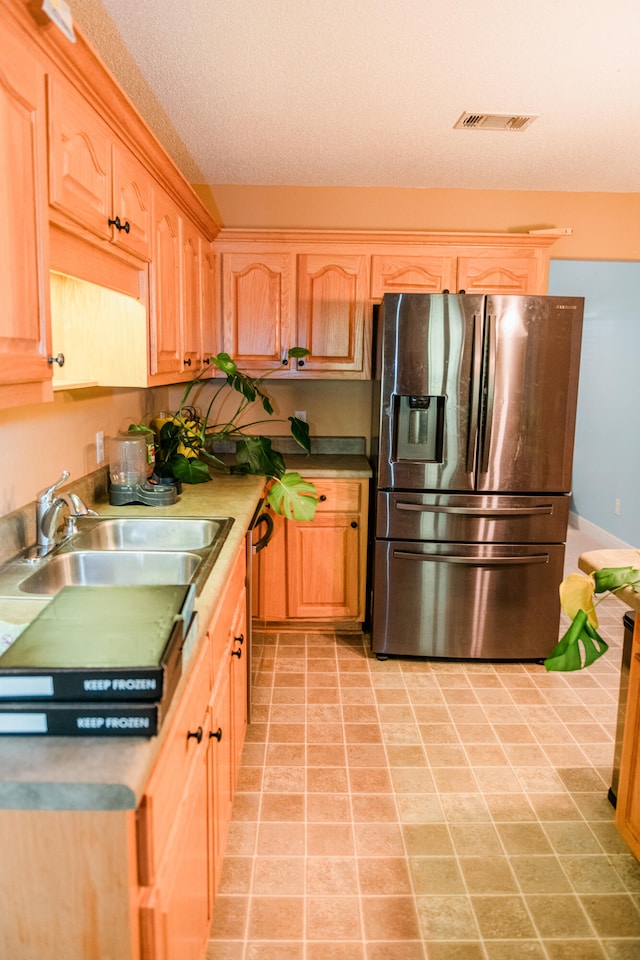 kitchen with stainless steel refrigerator with ice dispenser, sink, and a textured ceiling