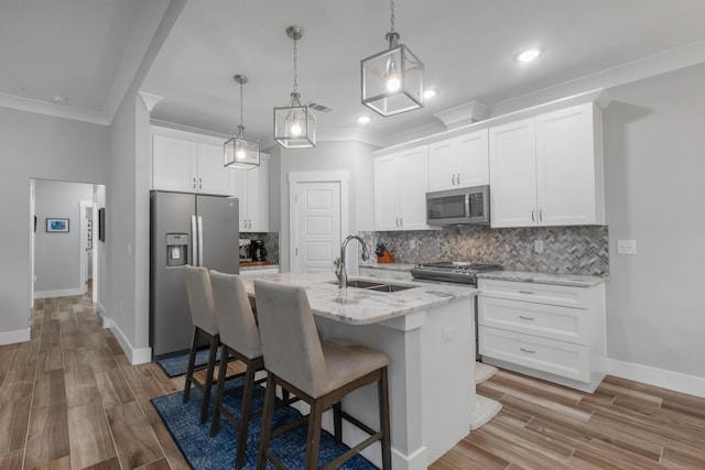 kitchen with a center island with sink, appliances with stainless steel finishes, decorative light fixtures, white cabinetry, and a sink