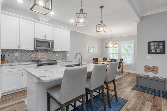 kitchen with an island with sink, decorative light fixtures, stainless steel appliances, white cabinetry, and a sink