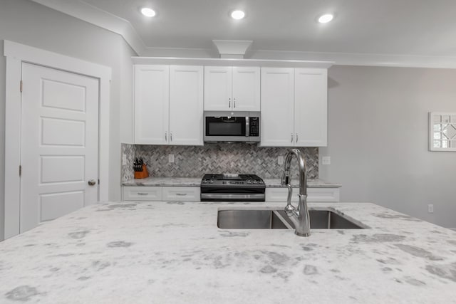 kitchen featuring appliances with stainless steel finishes, light stone counters, ornamental molding, white cabinetry, and a sink