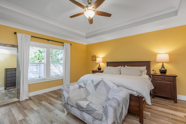 bedroom featuring a tray ceiling, light wood-style flooring, and baseboards