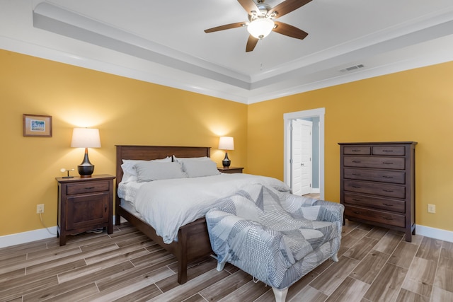 bedroom featuring a ceiling fan, baseboards, visible vents, wood tiled floor, and a tray ceiling