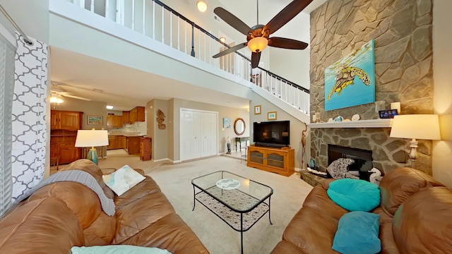 living room with ceiling fan, a towering ceiling, light colored carpet, and a fireplace