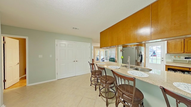 kitchen with a breakfast bar, sink, light stone counters, stainless steel fridge with ice dispenser, and a textured ceiling