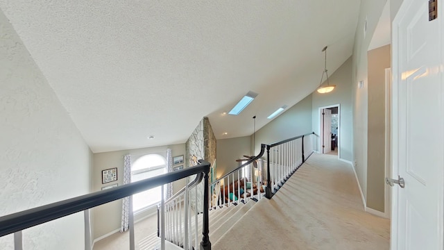 hallway featuring high vaulted ceiling, light carpet, a textured ceiling, and a skylight