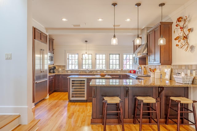 kitchen with beverage cooler, a kitchen bar, built in appliances, light stone counters, and kitchen peninsula