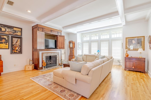 living room featuring beam ceiling, a tiled fireplace, coffered ceiling, and light hardwood / wood-style floors