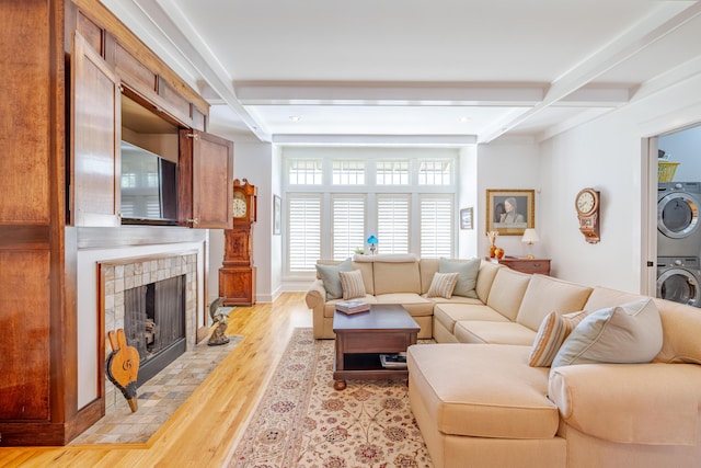 living room featuring stacked washer and dryer, coffered ceiling, light hardwood / wood-style flooring, a tile fireplace, and beamed ceiling