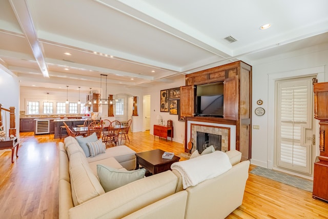 living room with wine cooler, a tiled fireplace, coffered ceiling, beam ceiling, and light hardwood / wood-style flooring