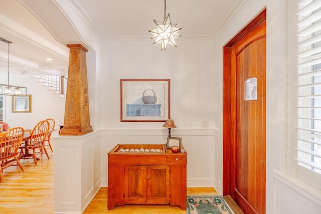 entrance foyer featuring decorative columns, ornamental molding, a notable chandelier, and light wood-type flooring