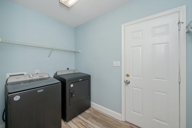 washroom with a textured ceiling, washing machine and dryer, laundry area, baseboards, and light wood finished floors