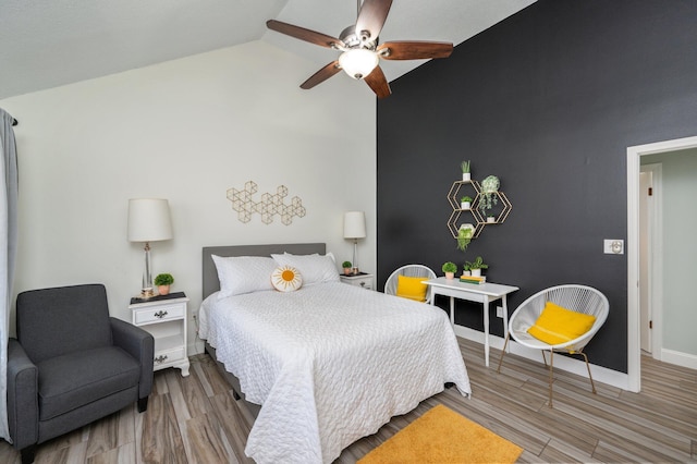 bedroom with lofted ceiling, light wood-style floors, an accent wall, ceiling fan, and baseboards