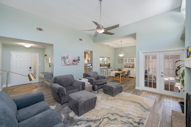 living room featuring light wood finished floors, french doors, a towering ceiling, and visible vents