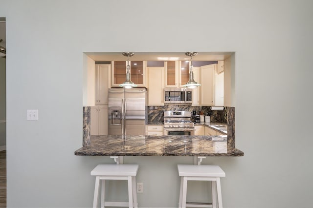 kitchen with pendant lighting, a breakfast bar area, stainless steel appliances, glass insert cabinets, and dark stone countertops