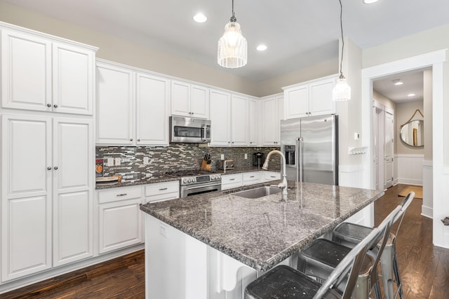 kitchen featuring appliances with stainless steel finishes, decorative light fixtures, white cabinetry, a breakfast bar area, and a center island with sink