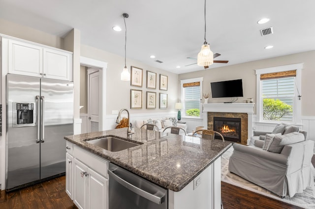 kitchen featuring sink, a center island with sink, dark stone countertops, stainless steel appliances, and white cabinets