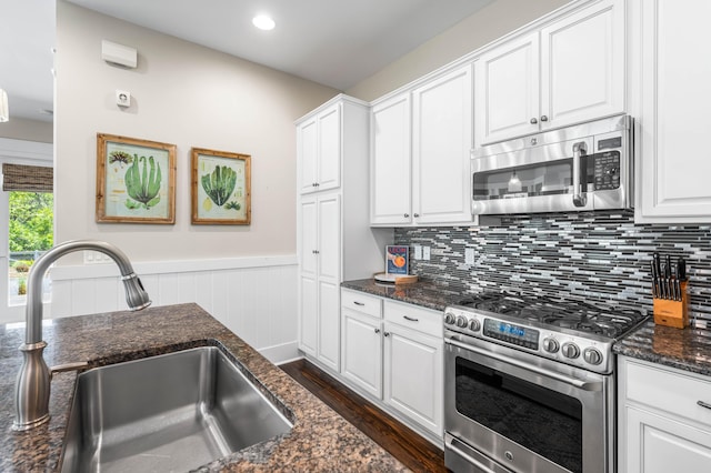 kitchen with sink, white cabinetry, dark stone counters, stainless steel appliances, and decorative backsplash