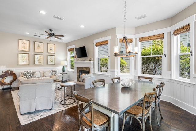 dining room featuring a tile fireplace, dark wood-type flooring, ceiling fan with notable chandelier, and a healthy amount of sunlight