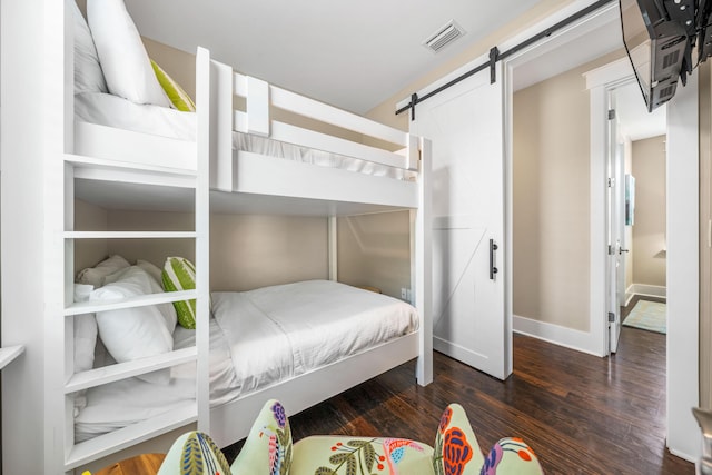 bedroom with a barn door and dark hardwood / wood-style floors