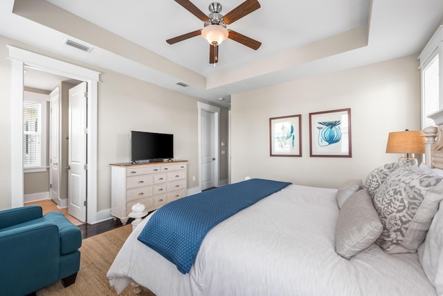 bedroom featuring multiple windows, hardwood / wood-style flooring, a raised ceiling, and ceiling fan