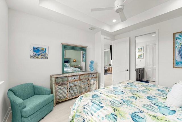 bedroom featuring a raised ceiling, ceiling fan, and ensuite bath